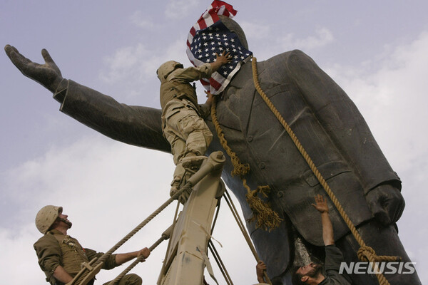 [바그다드( 이라크)=AP/뉴시스] 2003년  4월9일 이라크 침공 미군의 해병대 4연대 소속 에드워두 친 상병이 바그다드 시내의 거대한 사담 후세인 동상 철거를 위해 머리부분에 성조기를 씌우고 있다.